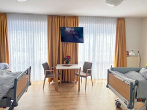 Aufenthalt im Zweibettzimmer mit bodentiefen Fenstern und einem Tisch mit zwei Stühlen