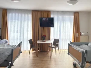 Aufenthalt im Zweibettzimmer mit bodentiefen Fenstern und einem Tisch mit zwei Stühlen